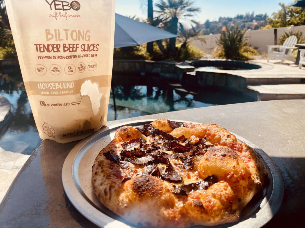 Fresh biltong pizza by the poolside with artisan beef slices and golden crust.