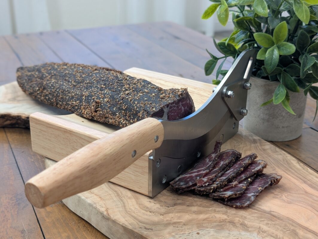 Rustic wooden biltong slicer cutting cured beef on a wooden table with natural lighting.