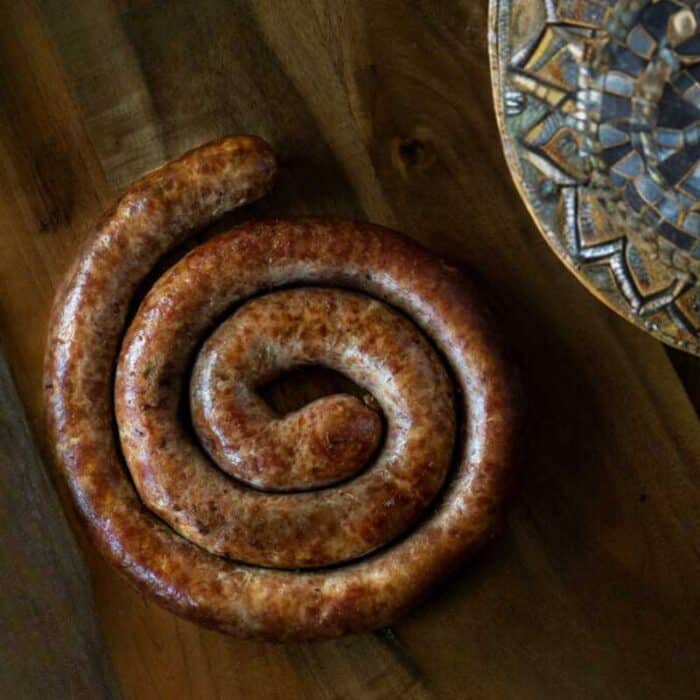 A boerewors farmers sausage coil on a table with a plate on the side