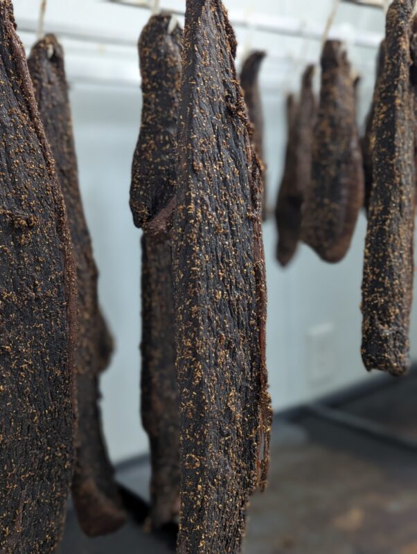 Homemade biltong - the health benefits of this snack 2 Hanging strips of seasoned beef biltong drying in a professional meat curing room.