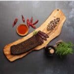 a piece of biltong slab on a cutting board with spices and herbs