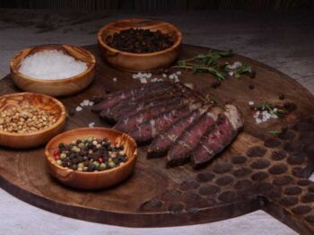 What is biltong? Sliced biltong on a wooden board with assorted spices and herbs.