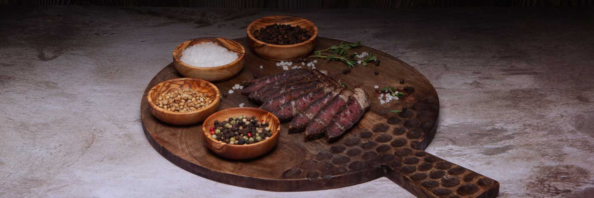 What is biltong? Sliced biltong on a wooden board with assorted spices and herbs.