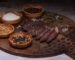 a cutting board with different bowls of spices and sliced biltong