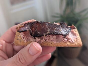 A slice of biltong protein snacks on top of pate and a wholewheat cracker