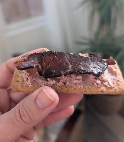 A slice of biltong protein snacks on top of pate and a wholewheat cracker
