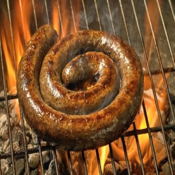 Coiled boerewors sausage grilling over open flames on a barbecue with glowing coals.