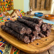 Traditional South African droëwors sausages on wooden platter with colorful African fabric background.