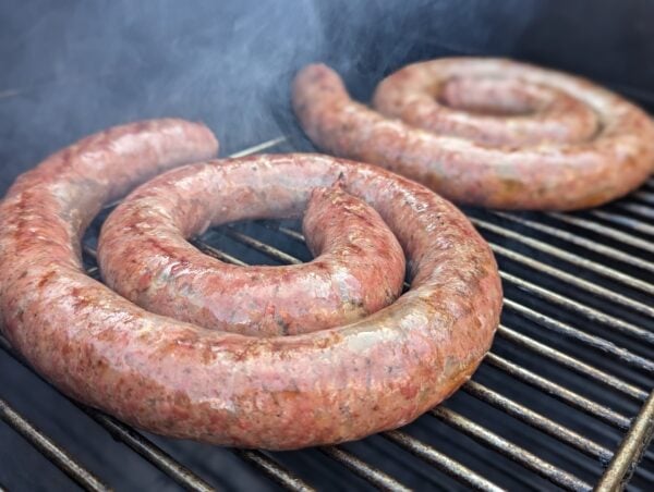 Coiled boerewors sausages grilling on barbecue with smoky flavor and golden-brown char.