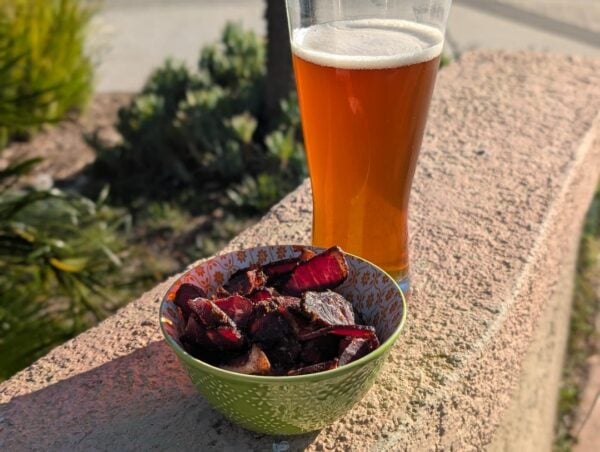 Biltong in patterned bowl with amber beer on stone ledge in sunlight.