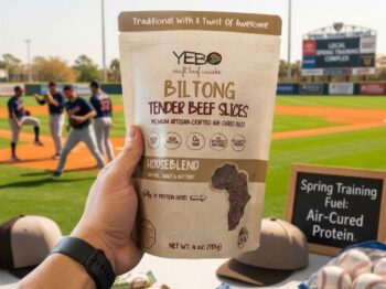 Hand holding YEBO Biltong beef snack at sunny baseball field during spring training.
