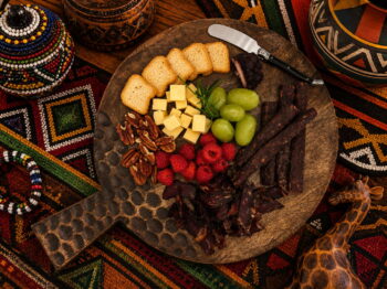 African charcuterie board with cheese, biltong, grapes, raspberries, and nuts on patterned fabric.