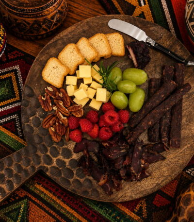 African charcuterie board with cheese, biltong, grapes, raspberries, and nuts on patterned fabric.