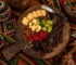 African charcuterie board with cheese, biltong, grapes, raspberries, and nuts on patterned fabric.
