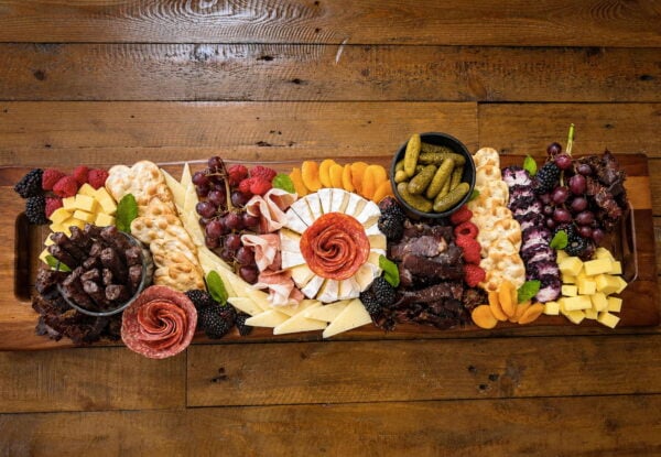 Colorful charcuterie board with cheeses, meats, fruits, crackers, and biltong on a rustic table.