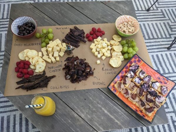 Rustic charcuterie board with biltong, cheese, fruit, and snacks on a wooden table.