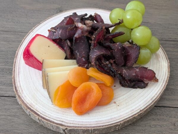 Charcuterie board with biltong, cheese, dried apricots, and fresh grapes on a rustic wooden platter.