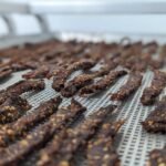 Homemade spicy beef jerky drying on a metal tray in a food dehydrator.