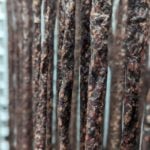 Hanging dried meat sticks and sausages in a curing rack for artisanal food preparation.