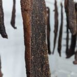 Hanging dried meat strips with seasoning in a curing room for jerky or biltong preparation.