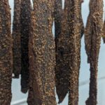 Hanging spiced dried meat strips coated with coarse seasoning in a curing or drying process.