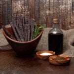 Rustic still life of cured meat sticks, herbs, salt, pepper, and sauce on wooden table.