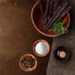 Rustic wooden bowls with beef jerky sticks, sea salt, chili flakes, and olive oil bottle.