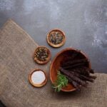 Rustic beef sticks with salt, peppercorns, and spices on burlap background.